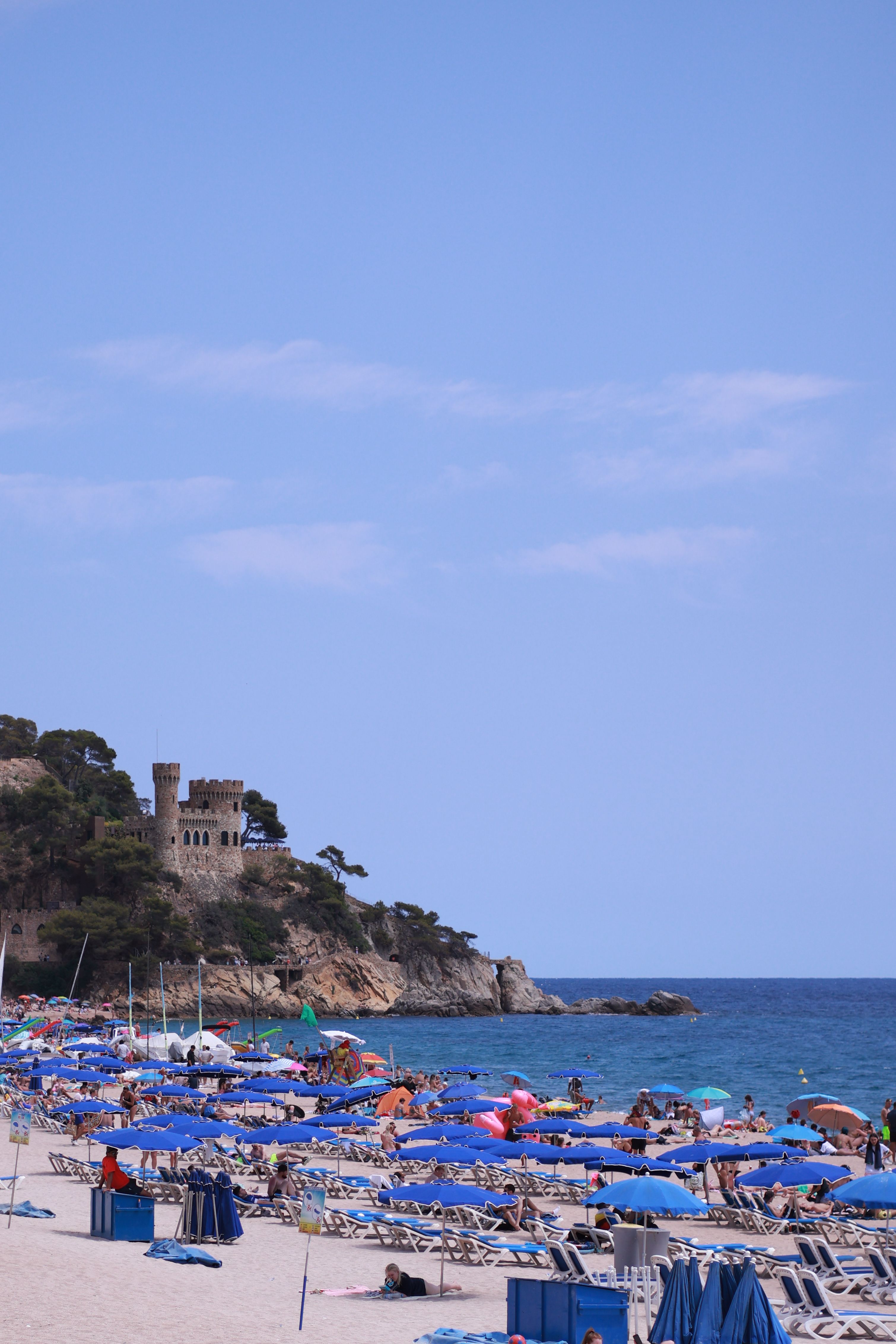Explore a vibrant beach scene beside a historic castle overlooking the sea, perfect for summer vacations.