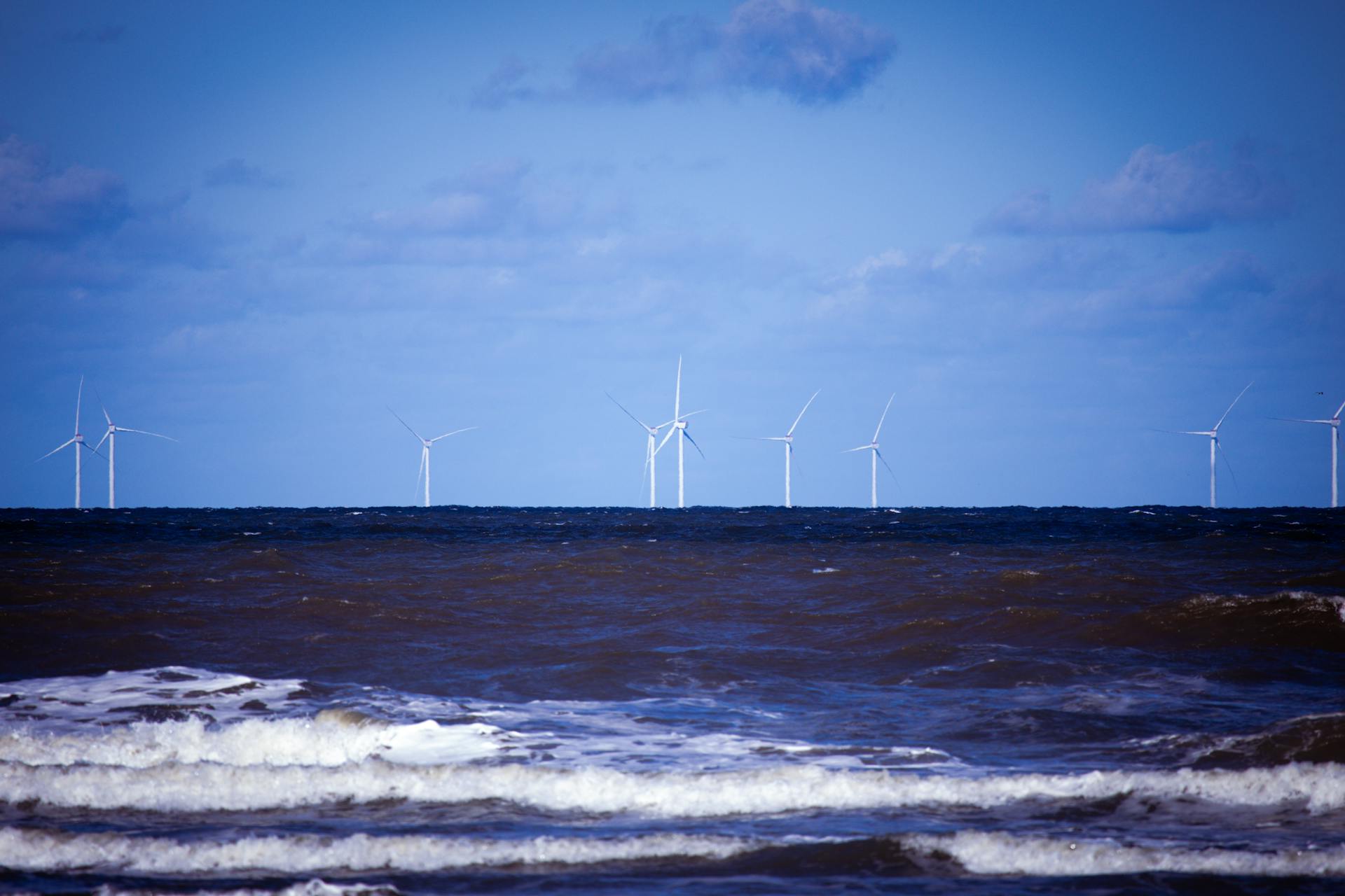 Offshore wind turbines generating sustainable energy over a calm ocean under a clear blue sky.
