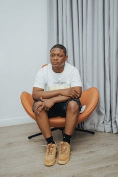 Young man in casual attire sitting in a modern orange armchair indoors.