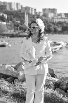 Fashionable woman in stylish attire holding bouquet near water, embracing summer's elegance.