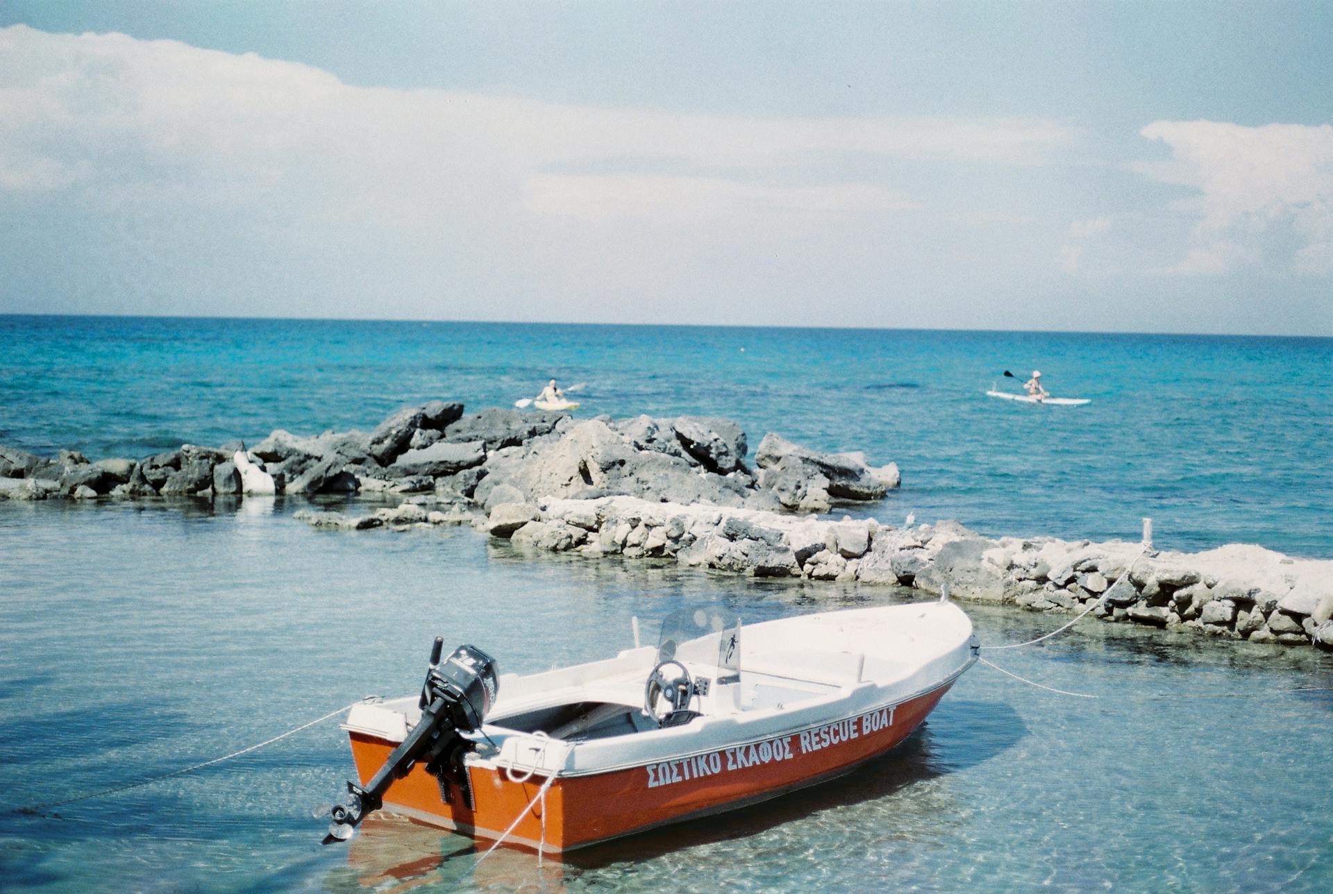 Peaceful scene of a moored rescue boat on a rocky shore with clear blue water.