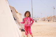 A young girl stands by a tent in a refugee camp in Idlib, Syria.