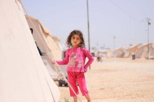 A young girl stands by a tent in a refugee camp in Idlib, Syria.
