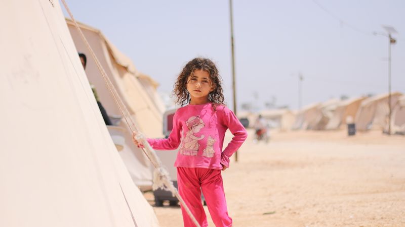 A young girl stands by a tent in a refugee camp in Idlib, Syria.