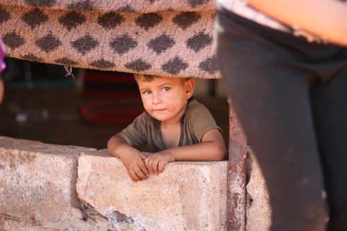 Free A young boy peeks out from under a blanket in a Syrian refugee camp, capturing innocence and resilience. Stock Photo