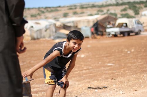 Free A smiling boy enjoys outdoor play in a rural Syrian landscape, embodying joy and resilience. Stock Photo