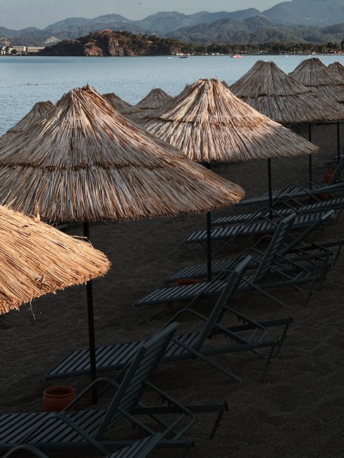 Peaceful beach scene with straw umbrellas and lounge chairs in Fethiye, Türkiye.