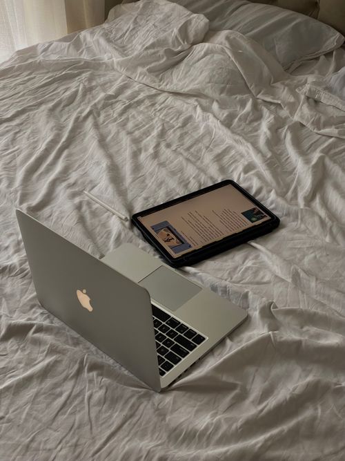 Free Minimalist workspace featuring a laptop and tablet on an unmade bed, depicting a casual work environment. Stock Photo