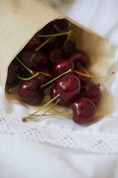 A rustic display of juicy, fresh cherries spilling from a paper bag onto elegant white fabric.