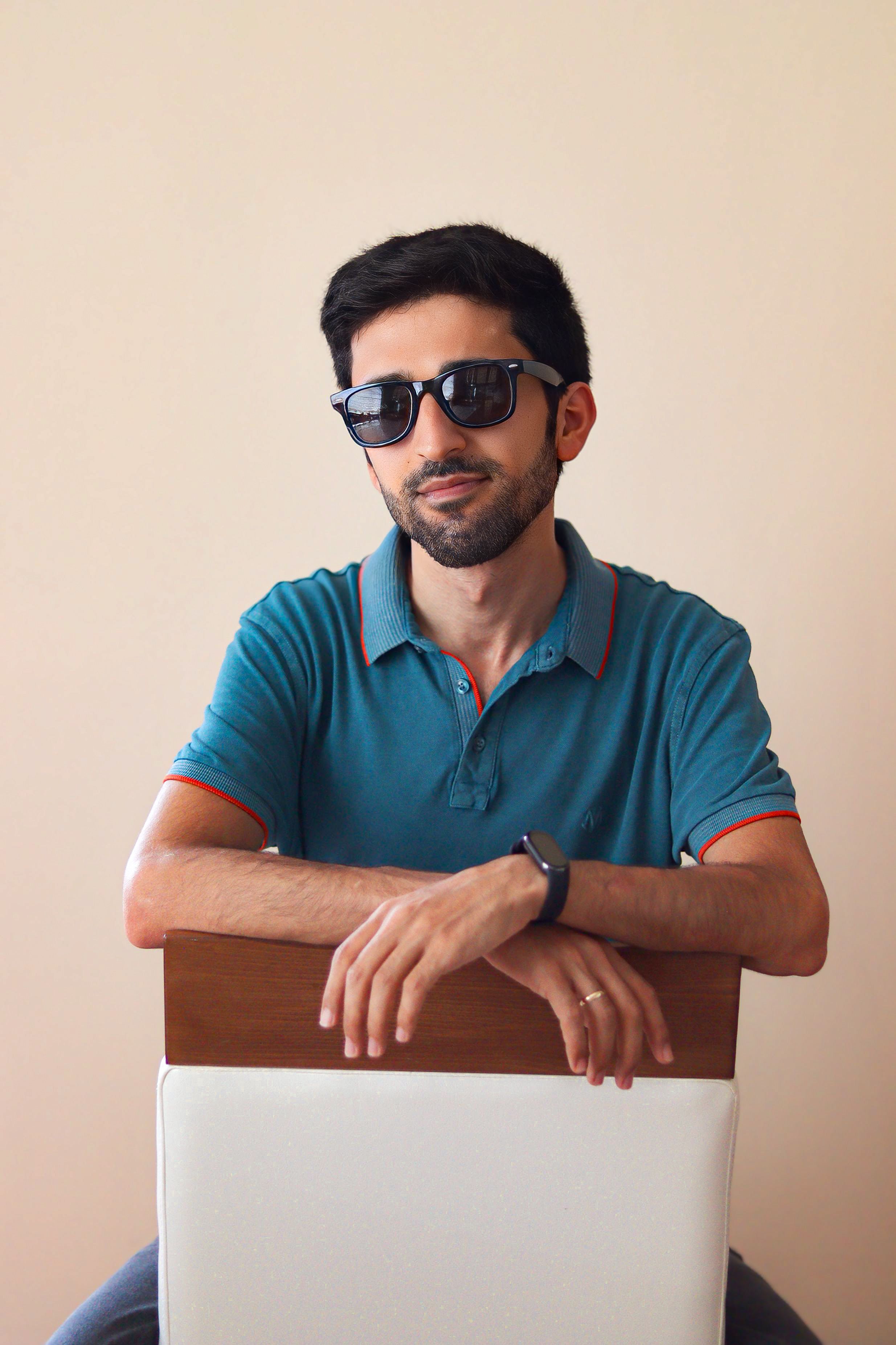 Stylish adult man with sunglasses seated indoors, exuding a modern and trendy vibe.