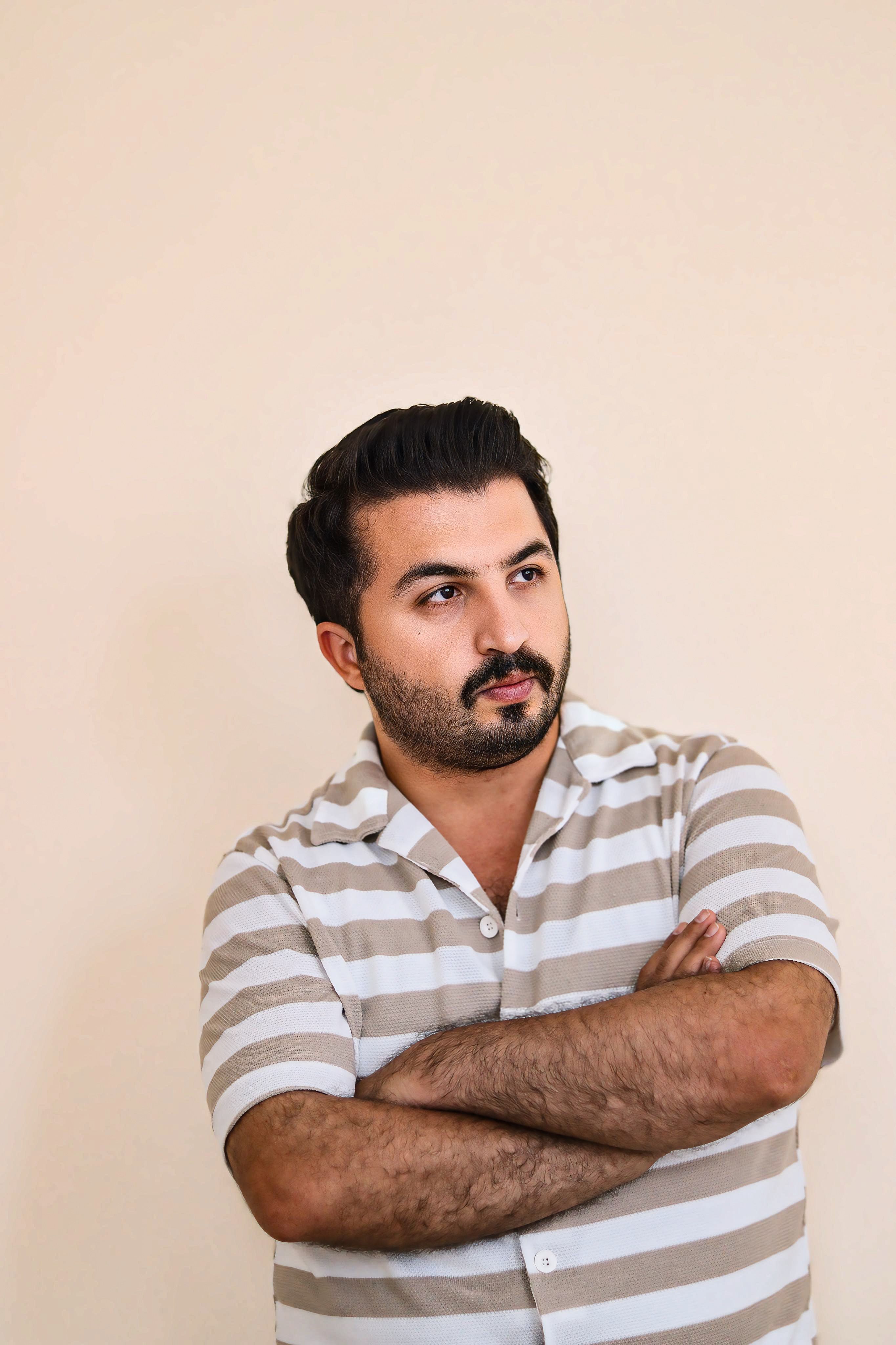 Pensive man with crossed arms looking away, wearing a striped shirt.