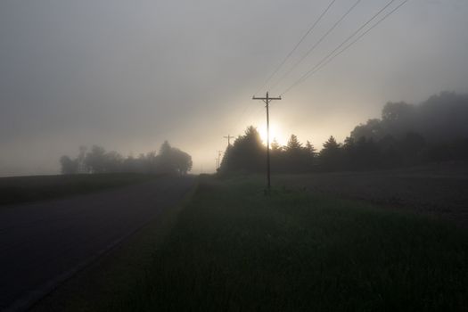 A misty sunrise over a rural road with silhouetted trees and fog in Wisconsin.