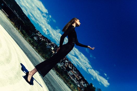 Elegant woman in black dress posing in a dynamic outdoor scene under a vibrant blue sky.