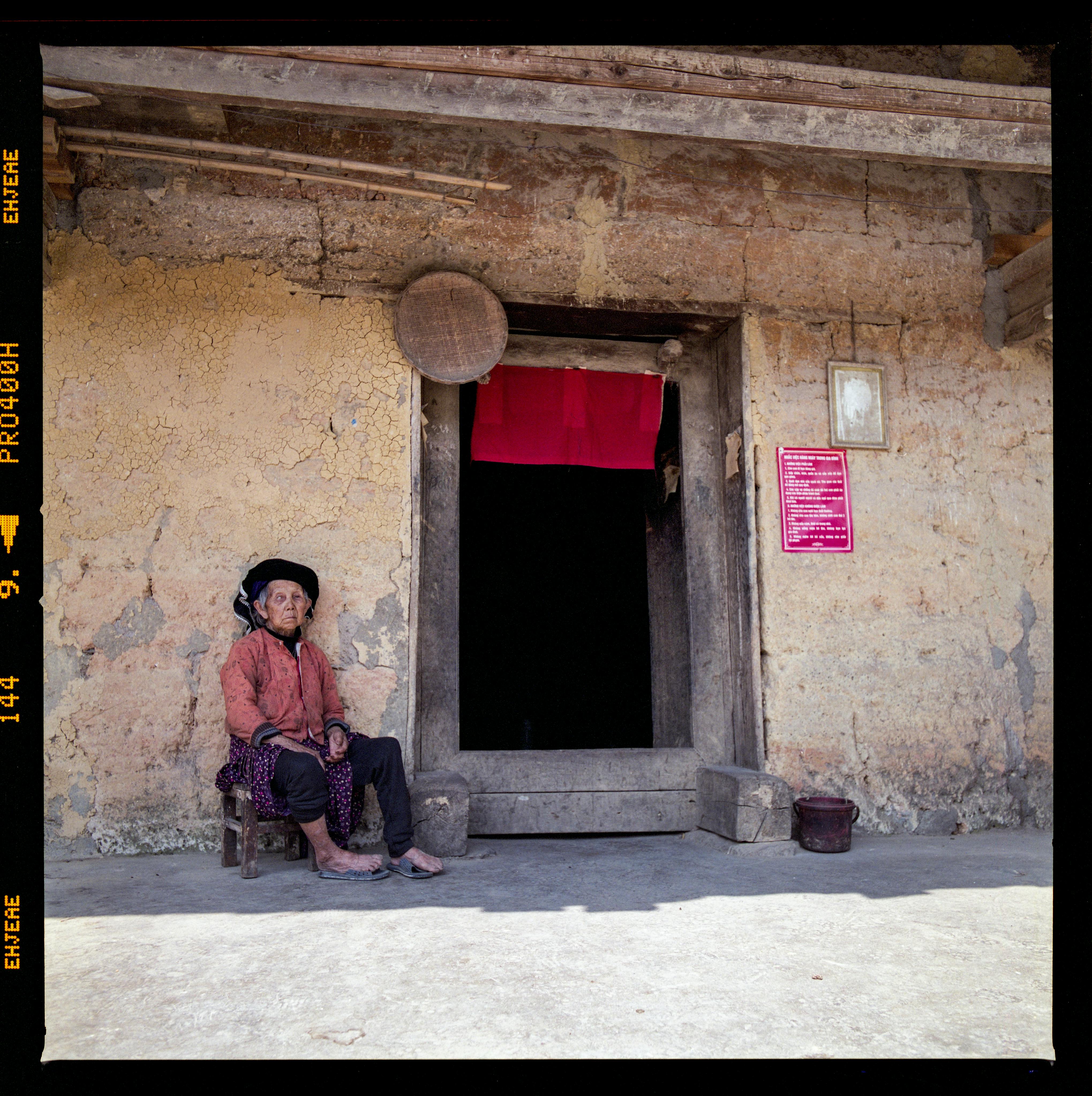 elderly woman sitting near village house entrance