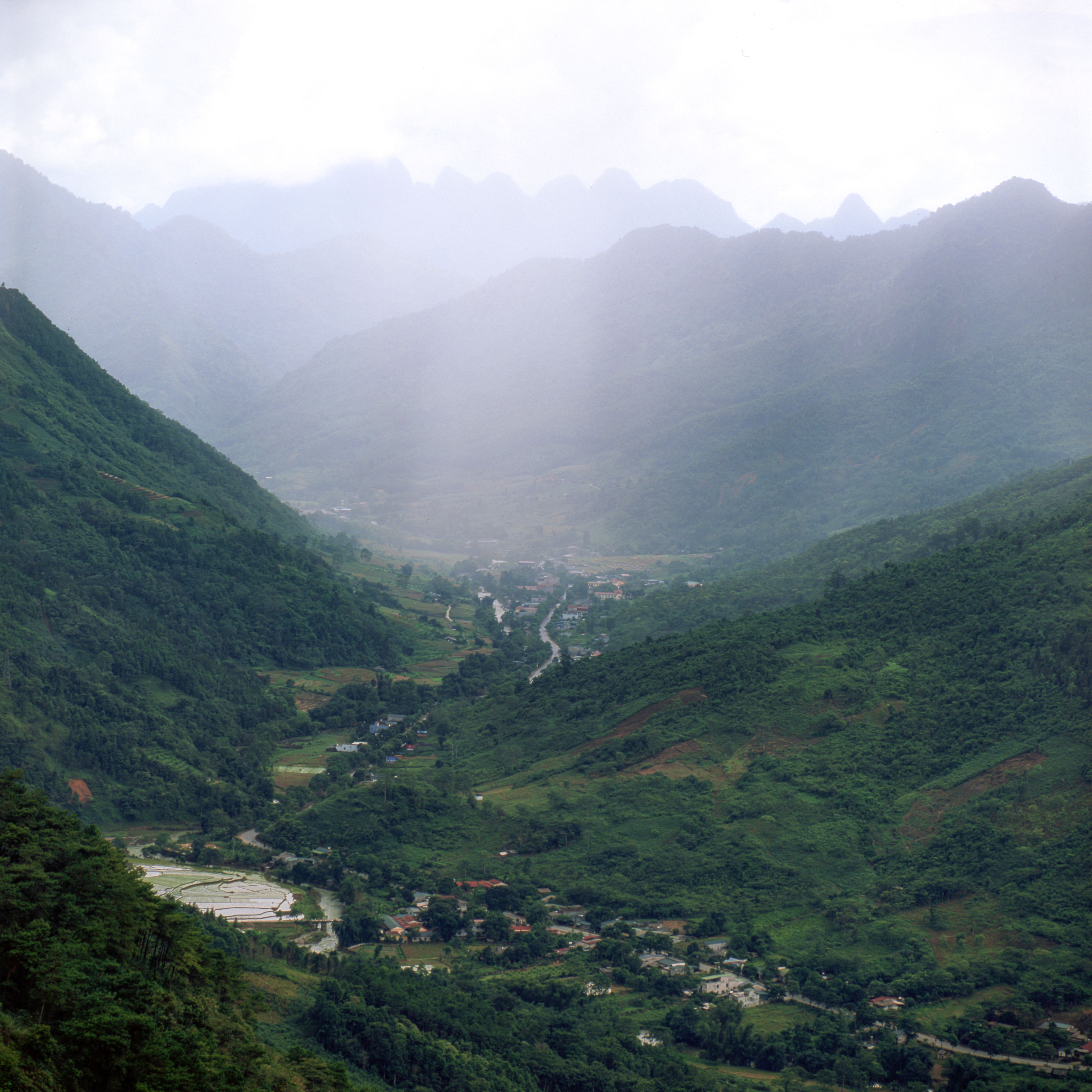 A serene view of a green mountain valley with mist and a snaking river.