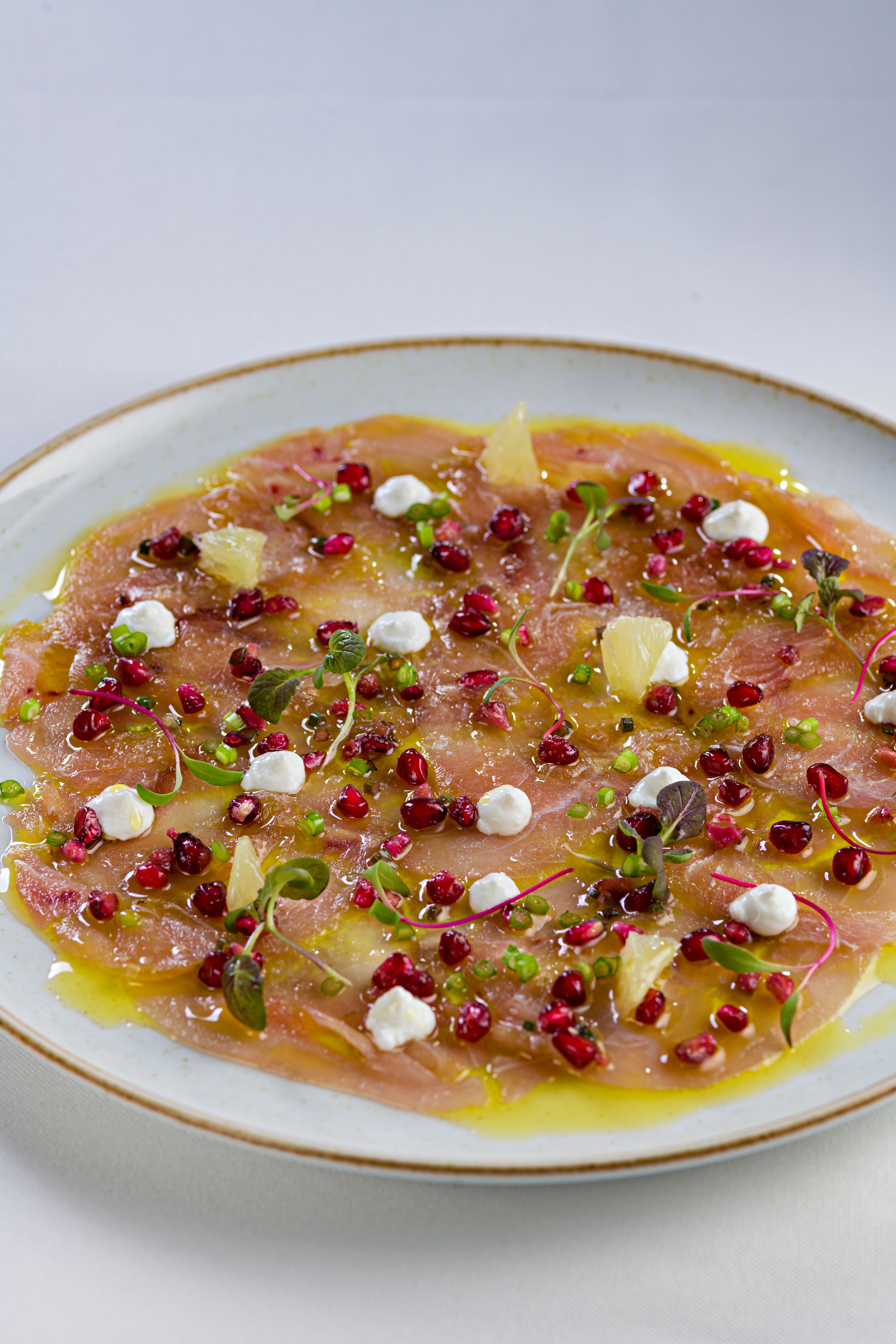 Elegant carpaccio dish topped with pomegranate seeds and citrus zest, perfect for gourmet dining.