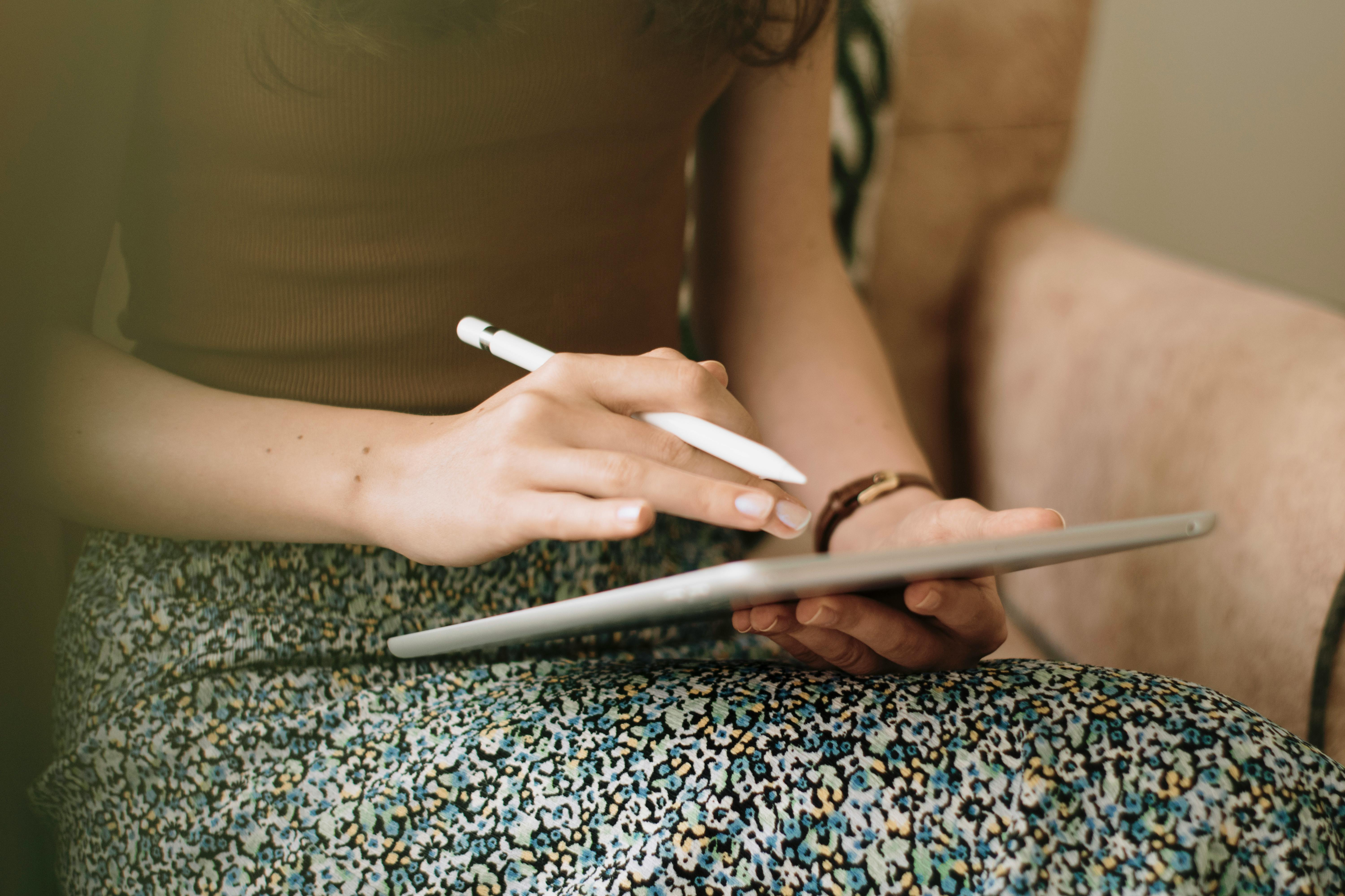 Close-up of a woman using a stylus pen on a digital tablet indoors.