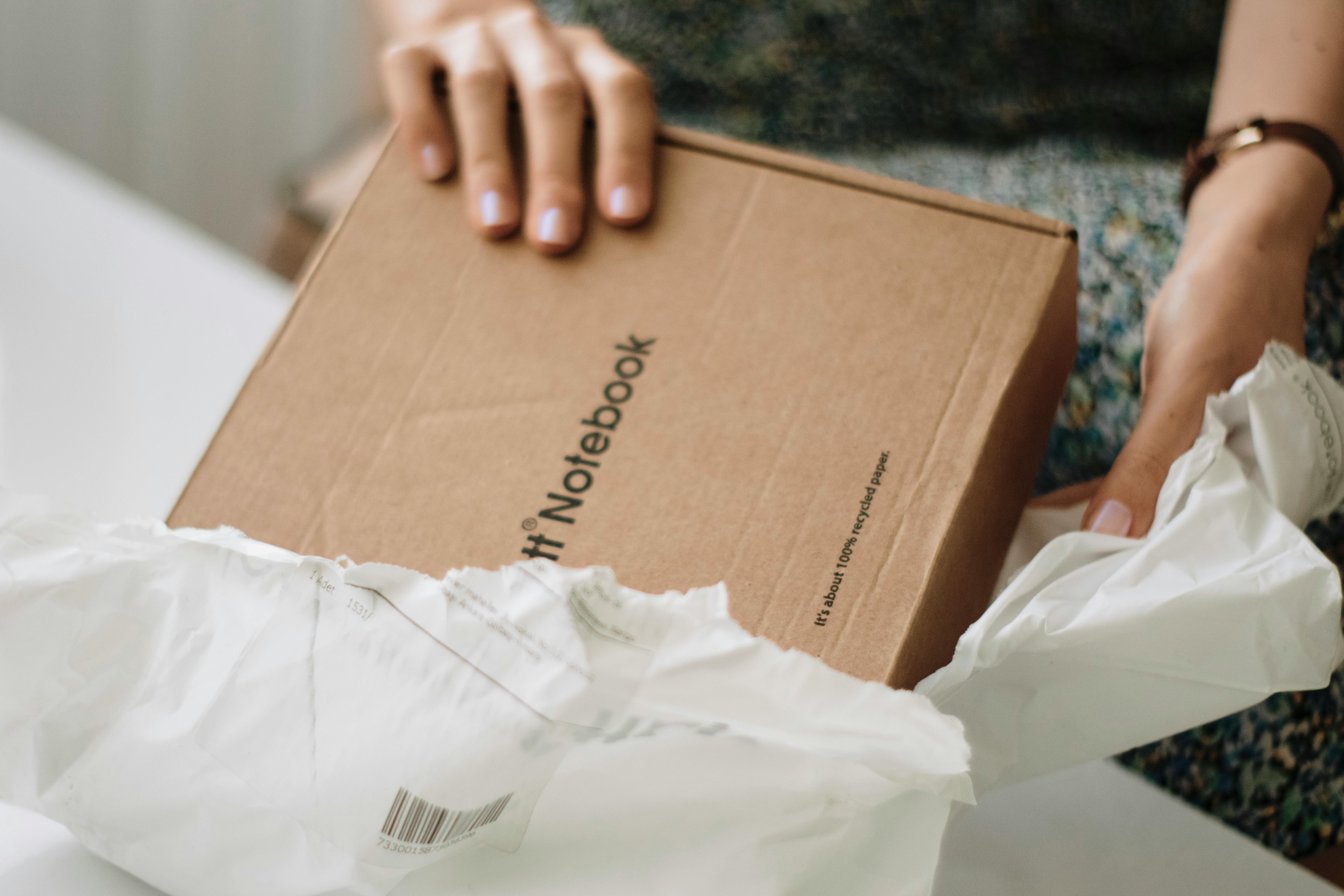 Woman unpacks a cardboard notebook in a cozy indoor setting, promoting eco-friendly packaging.