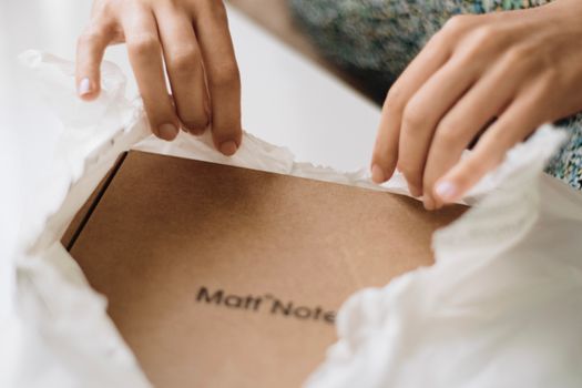 Close-up shot of hands unwrapping a brown cardboard box on white paper, suggesting a personal touch.