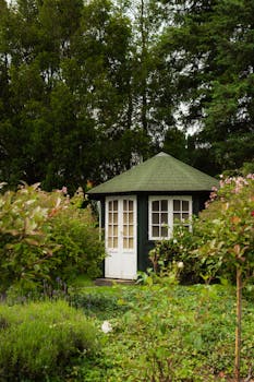 A picturesque dark green gazebo nestled in a lush, flowering garden.