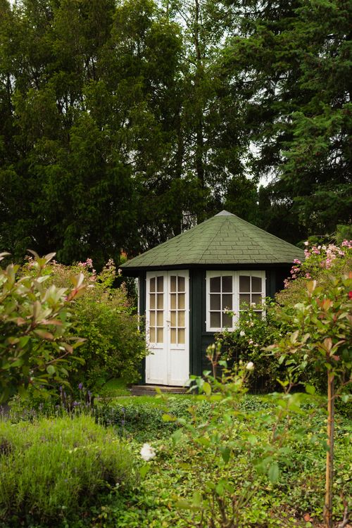Free A picturesque dark green gazebo nestled in a lush, flowering garden. Stock Photo