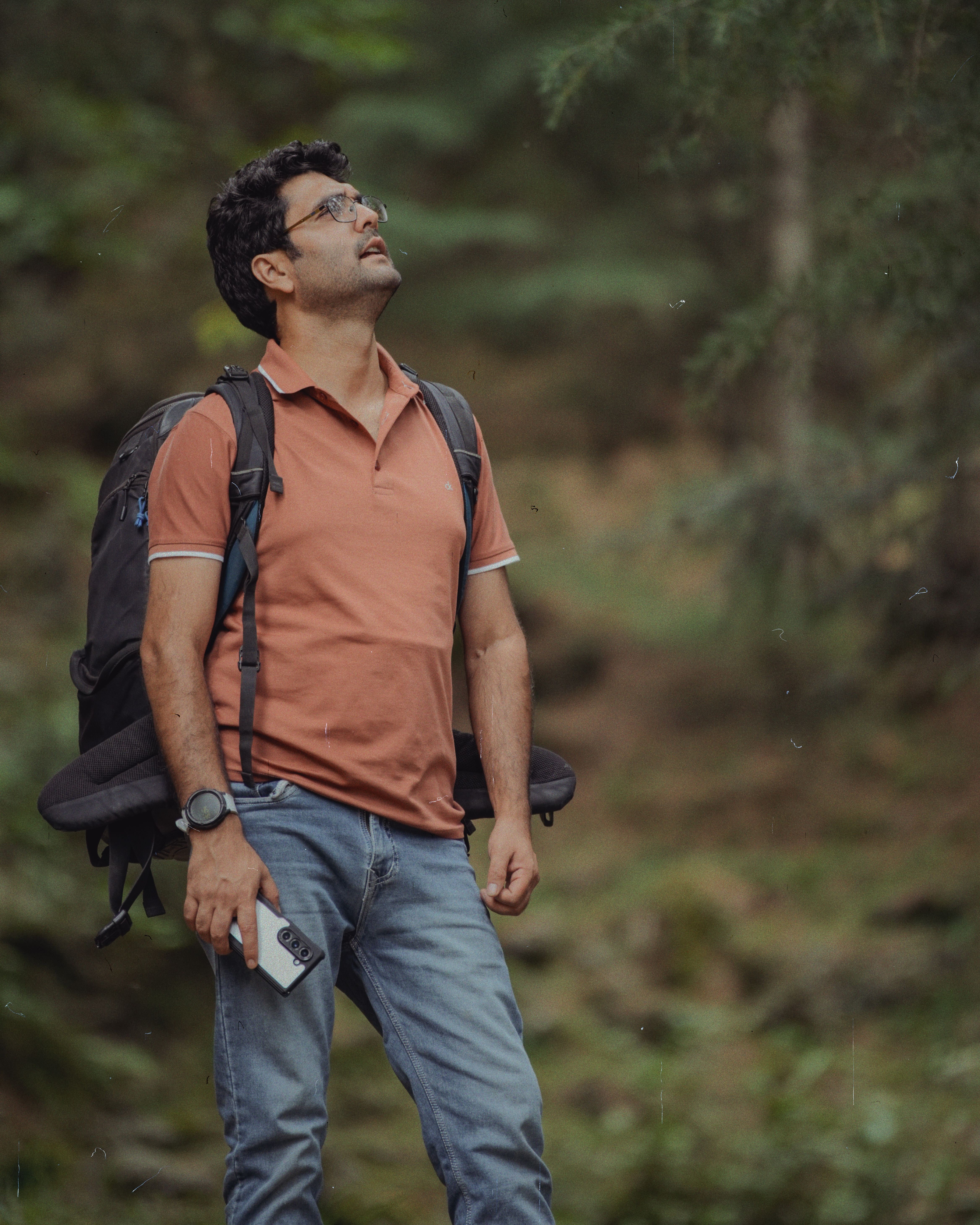 Casual hiker with backpack and smartphone exploring a lush green forest.