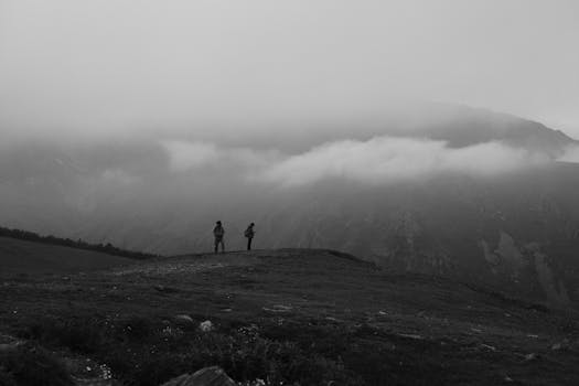 Black and white image of two hikers on a misty mountain landscape.
