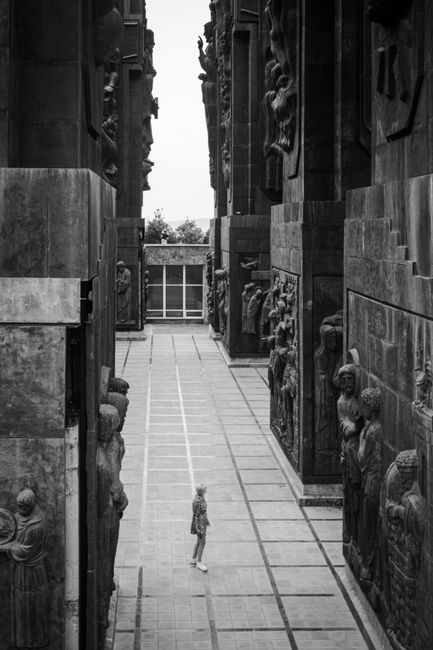 A person walking in a sculpture-lined corridor, captured in black and white.