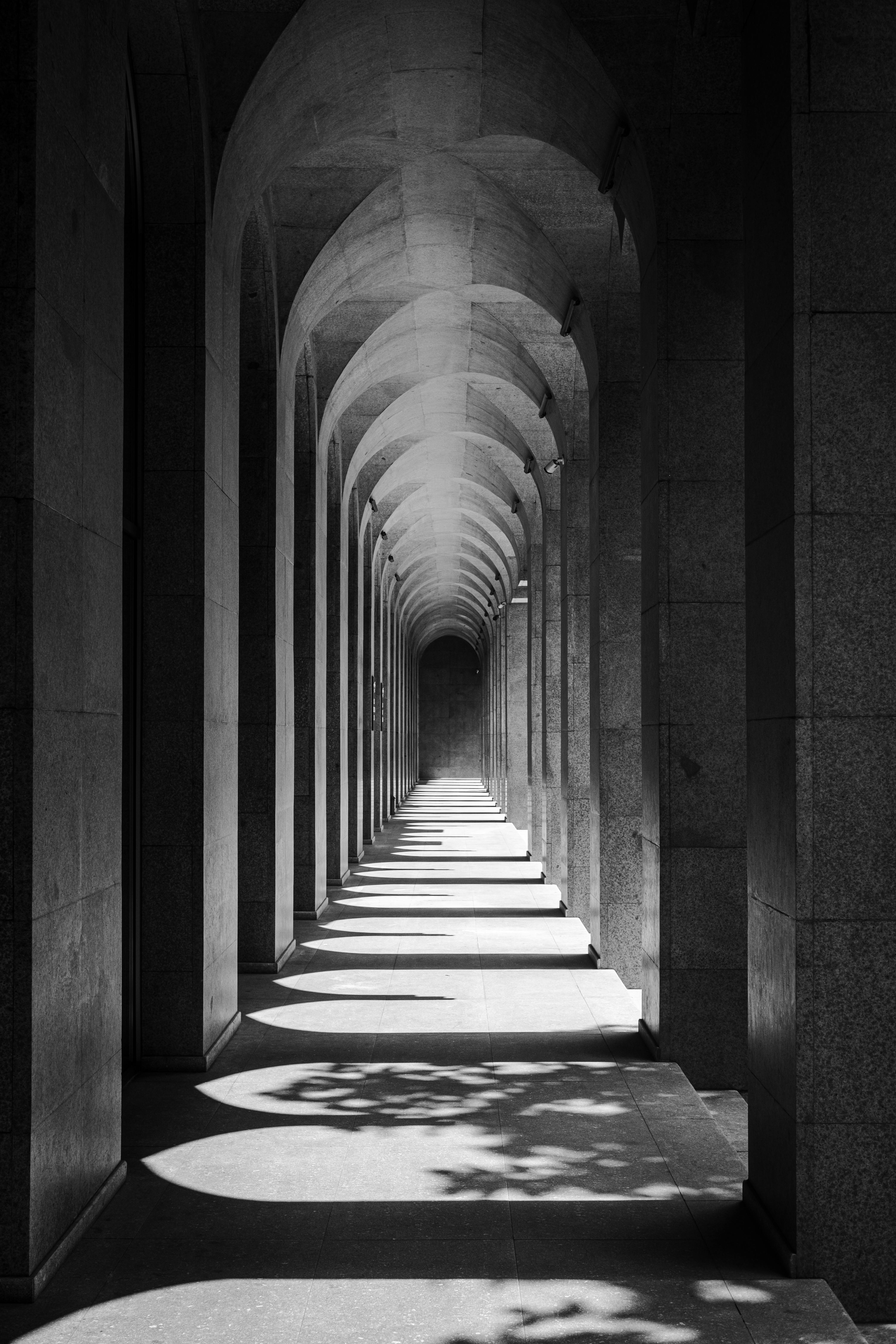 Black and white photo of a serene arched hallway with intricate shadows.