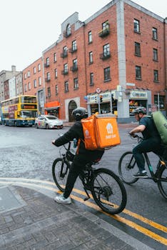 Two cyclists with delivery bags navigate through Dublin's urban streets, showcasing a bustling city environment.