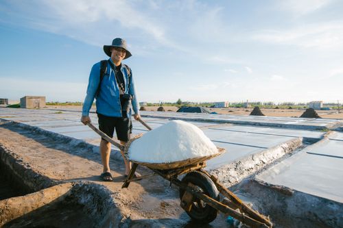 Free A man pushing a wheelbarrow full of salt at a salt flat on a sunny day, smiling and wearing a sun hat. Stock Photo