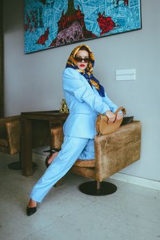 Fashionable woman in a blue suit and scarf posing indoors with modern art.