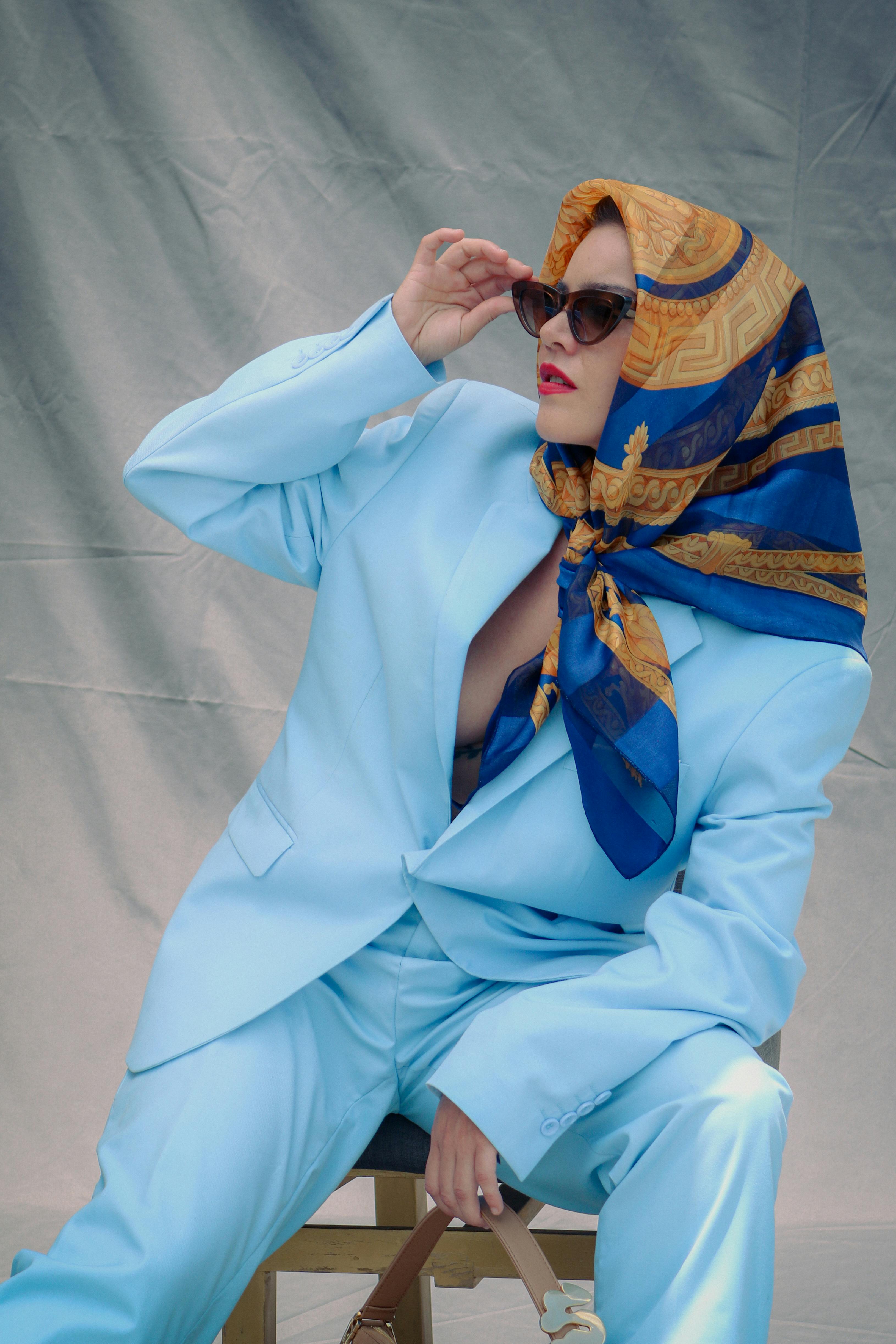 Free Stylish woman in a vibrant blue suit and scarf, posing elegantly with sunglasses. Stock Photo