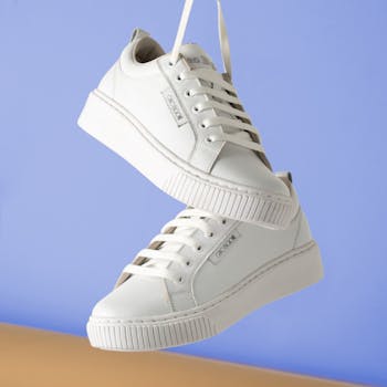 Minimalist white sneakers hanging against a soft blue backdrop for fashion product focus.