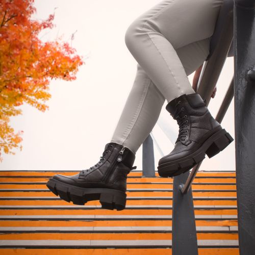Free Stylish black boots paired with white pants on a staircase accentuated by vibrant autumn leaves. Stock Photo