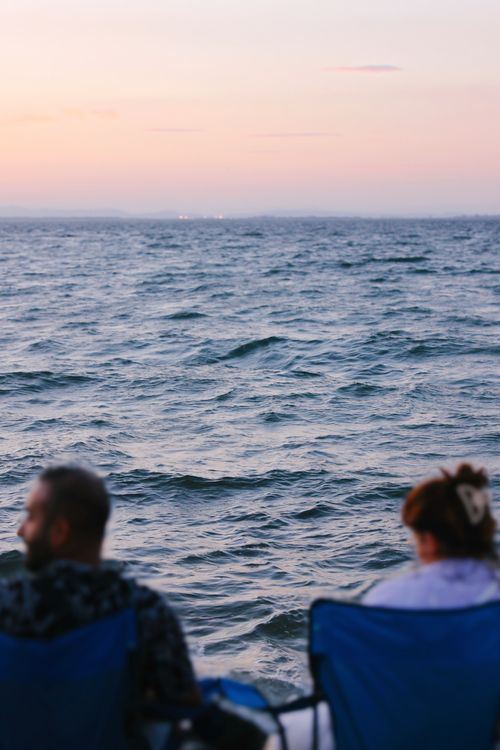 Free Two people enjoy a serene sunset by the ocean, perfect for relaxation. Stock Photo