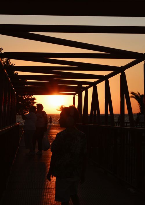 Free Silhouettes of people walking on a bridge during a beautiful sunset by the beach. Stock Photo