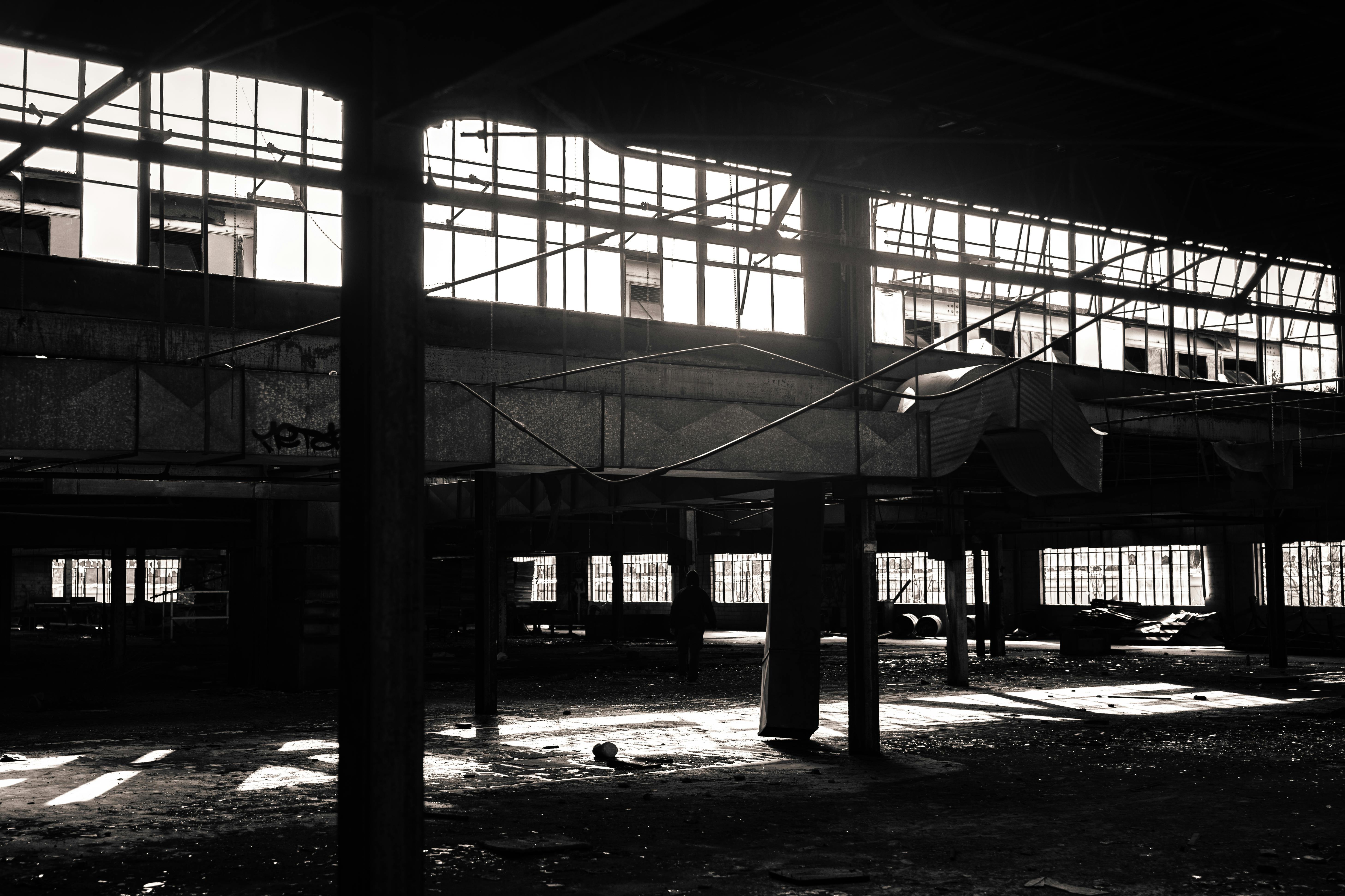 A moody black and white image of a decaying abandoned warehouse interior.