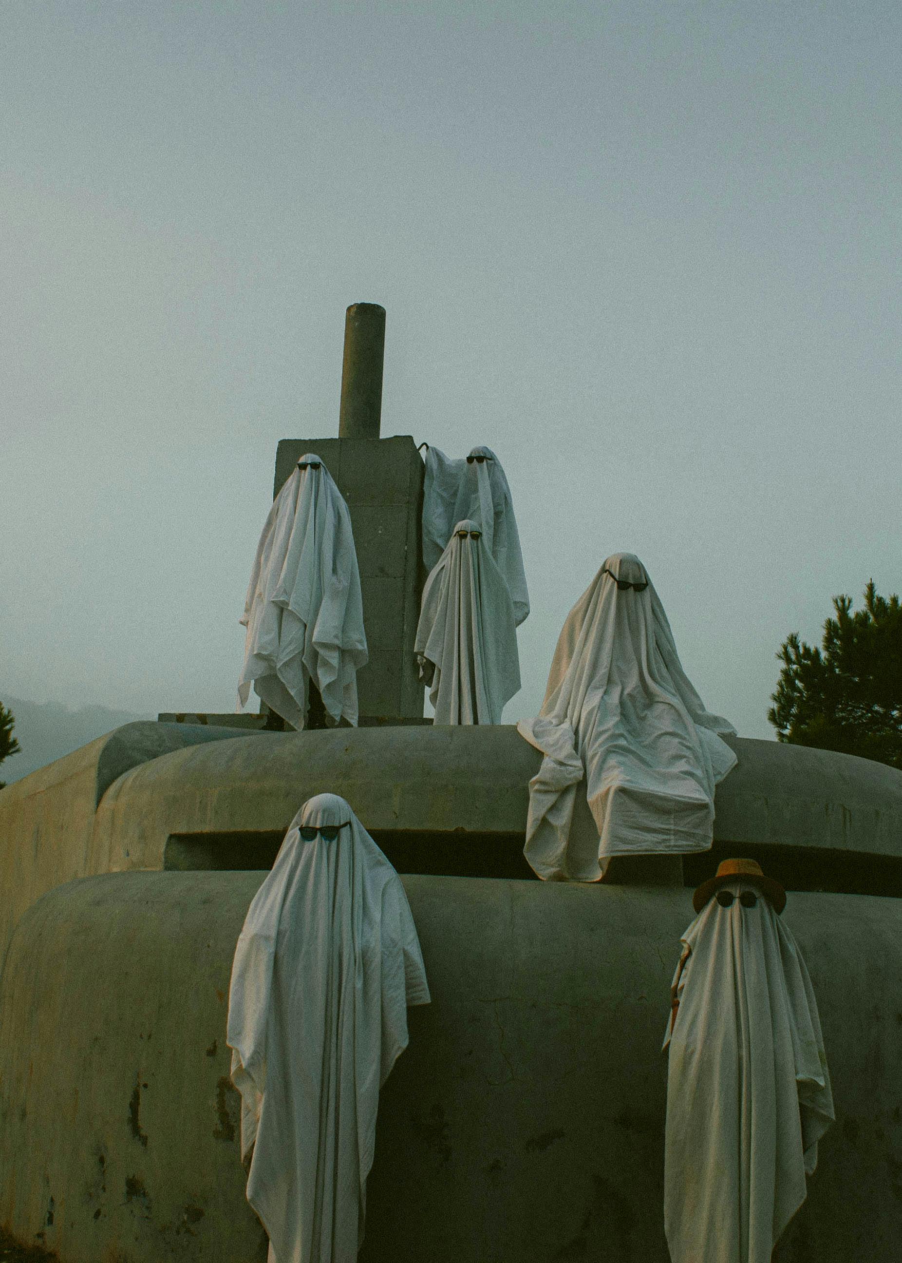 Eerie scene with ghostly figures draped in white sheets on an outdoor monument.