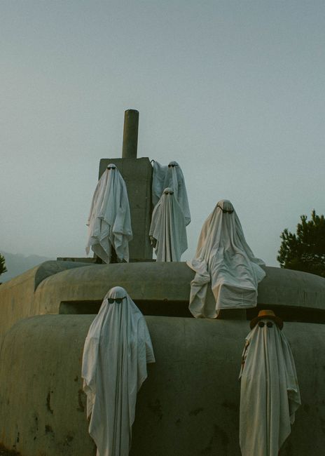 Eerie scene with ghostly figures draped in white sheets on an outdoor monument.