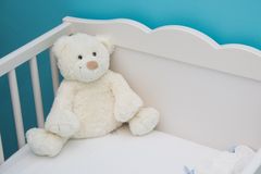 Soft teddy bear in a white crib against a vibrant blue wall, creating a comforting nursery atmosphere.