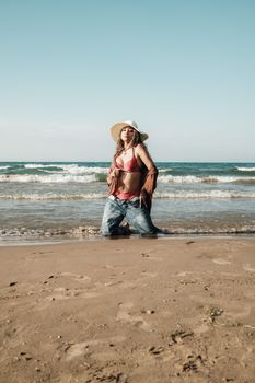 Woman kneeling on the beach wearing a bikini and sunhat against a clear blue sky.