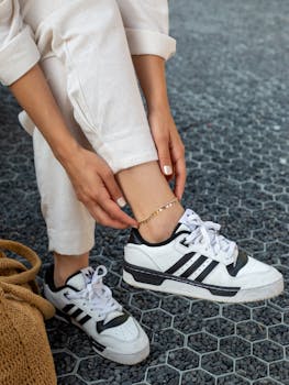 Close-up of woman adjusting her gold bracelet, wearing white sneakers and casual outfit outdoors.