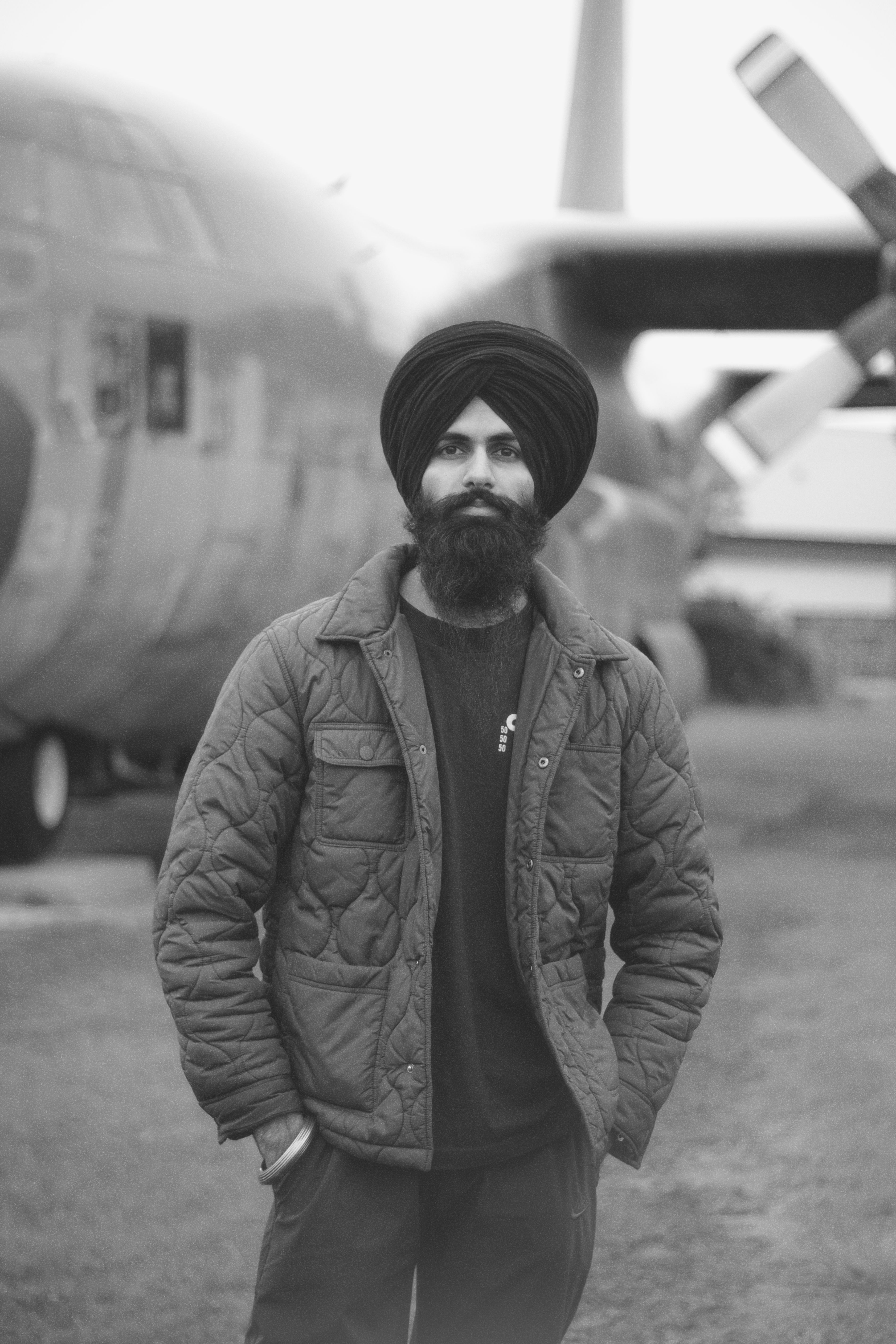 Black and white portrait of a Sikh man with a turban, standing outdoors by an aircraft in Toronto.