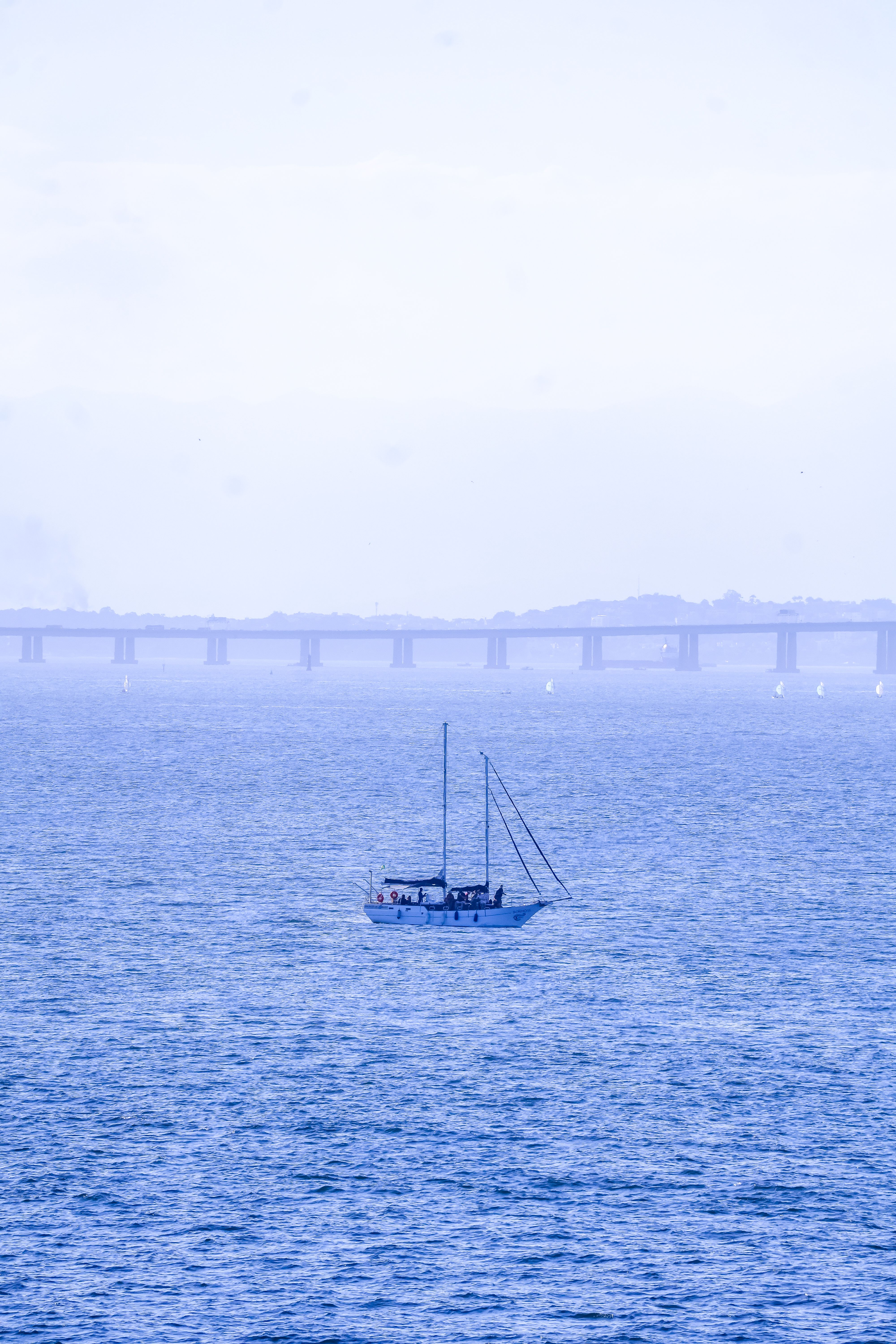 A serene sailboat on Guanabara Bay with the Rio-Niterói Bridge in Niterói, Brazil in the background.