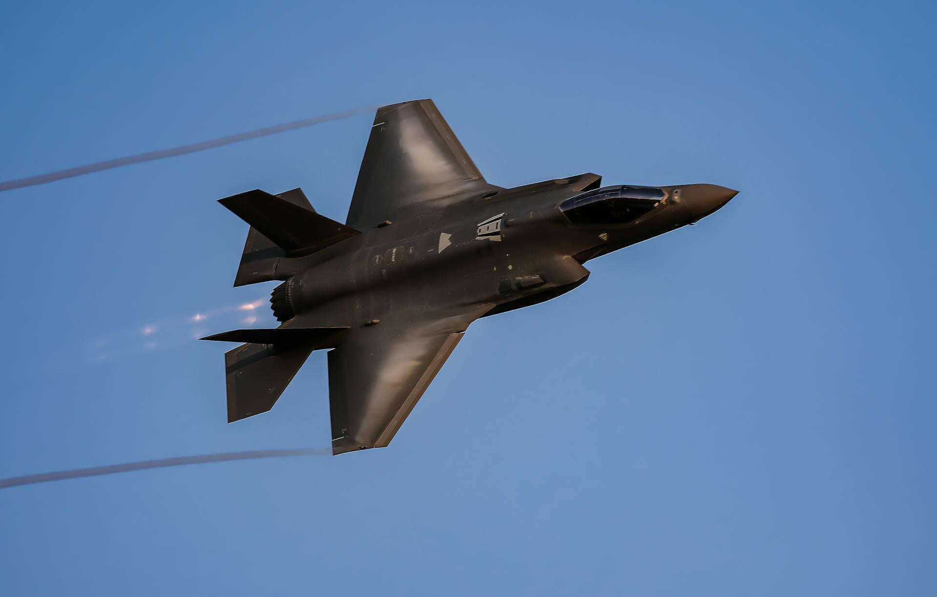 A sleek military fighter jet flying smoothly against a clear blue sky.