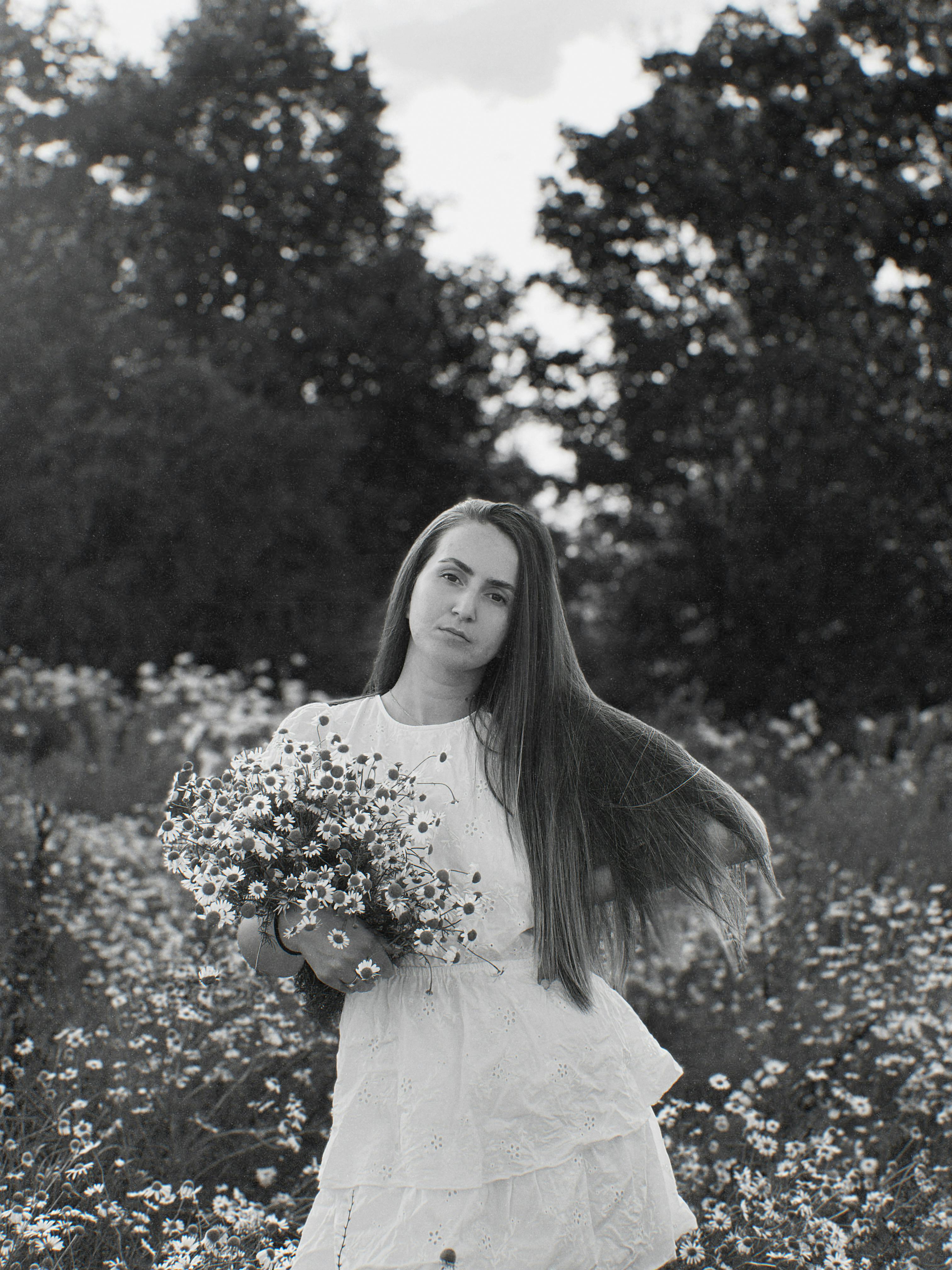 Black and white portrait of a woman in a meadow holding daisies, showcasing elegance and nature.