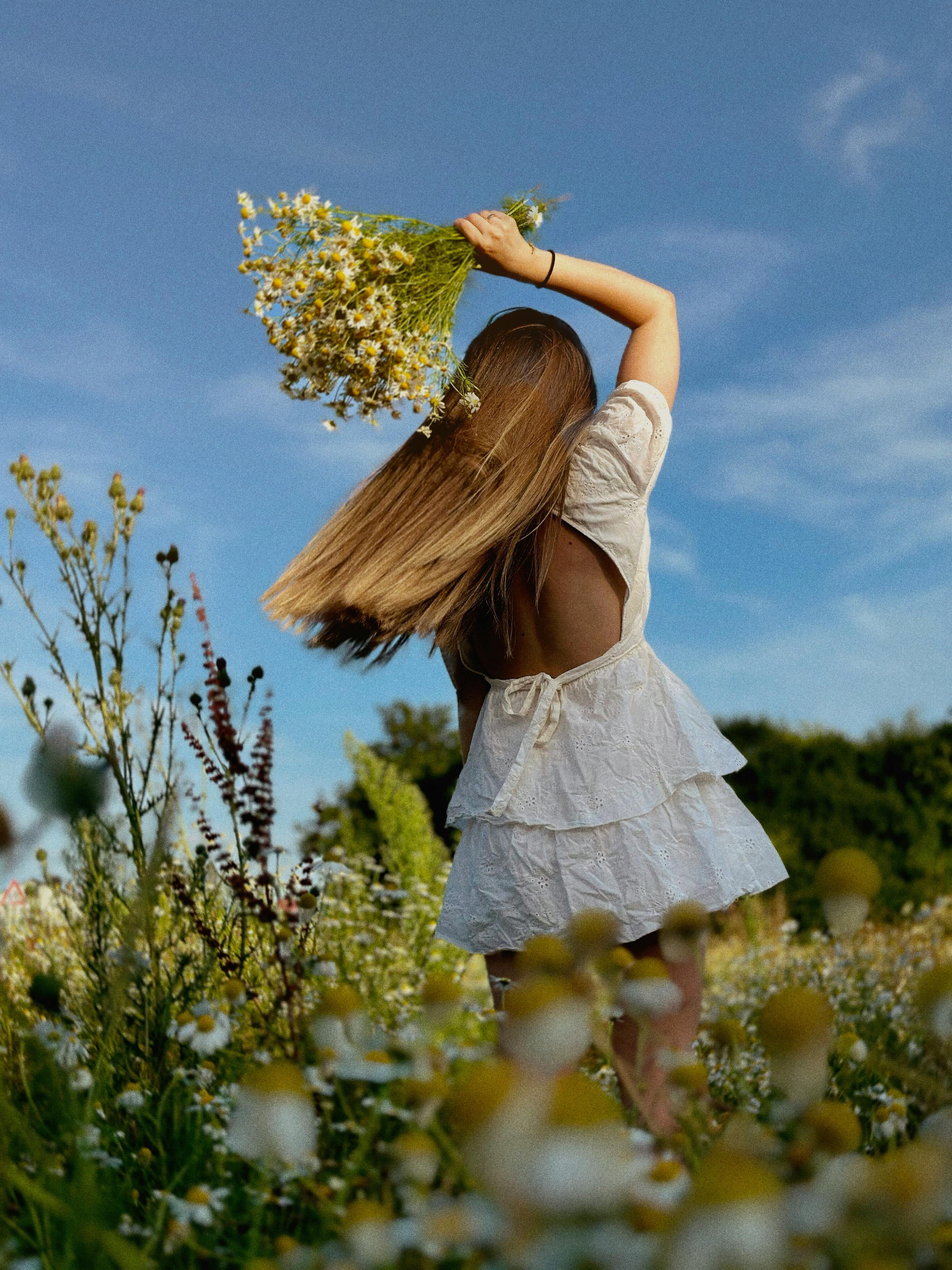 Woman in a white dress dancing in a sunny flower meadow.