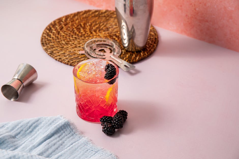 Colorful blackberry lemon cocktail with ice on a pink surface, perfect for summer gatherings.