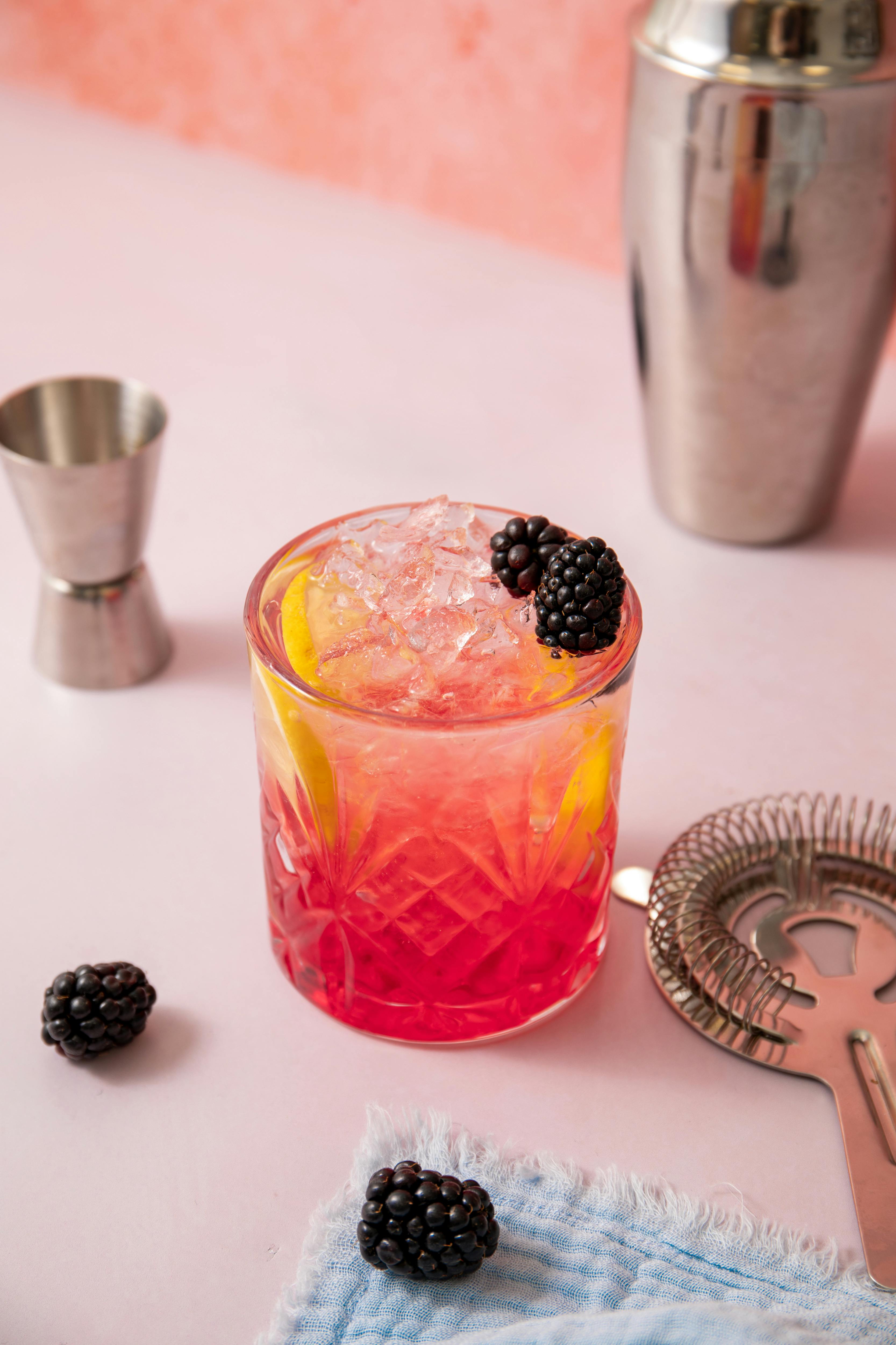 Delicious homemade blackberry cocktail with lemon slices in a crystal glass on a pink background, ideal for refreshment.